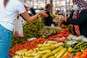 Colorful scene of a customer buying fresh vegetables from a vendor at a bustling farmers market.