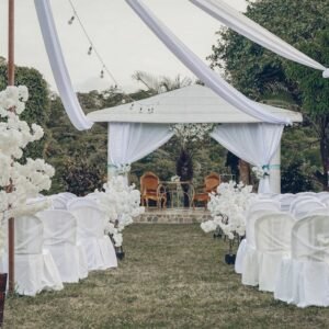 Charming outdoor wedding ceremony arrangement featuring white chairs, floral decorations, and a gazebo.