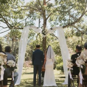 A beautiful outdoor wedding ceremony under a decorated tree with guests in attendance.