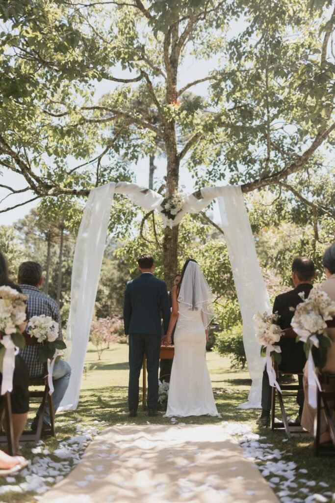 A beautiful outdoor wedding ceremony under a decorated tree with guests in attendance.