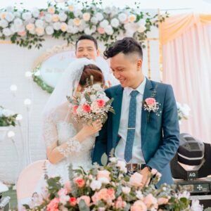 Newlyweds smiling amid lush floral arrangements during a bright wedding ceremony.