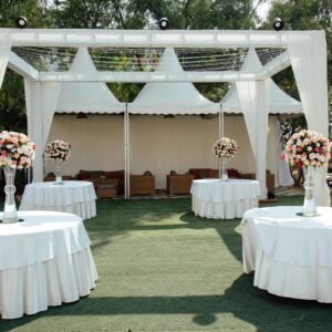 Charming outdoor wedding setup with white draped pergolas and floral centerpieces under a sunny sky.